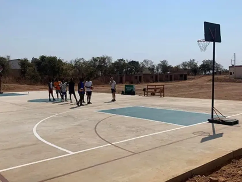 Outdoor concrete basketball court with portable hoop and group of people near center court