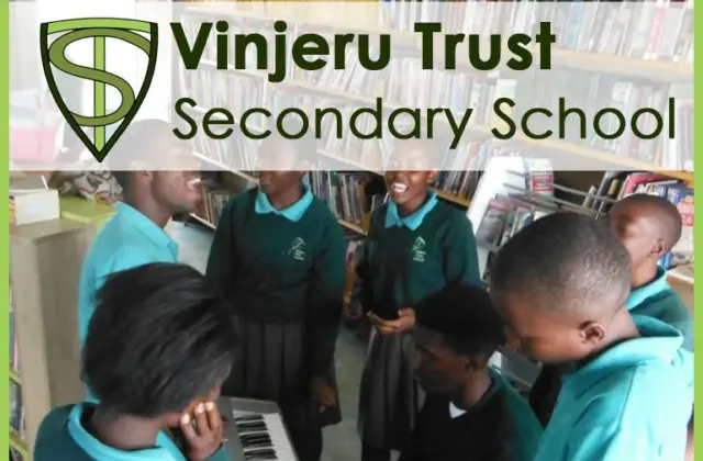 Students in teal uniforms gathered around a keyboard in a library, one student playing while others watch and sing