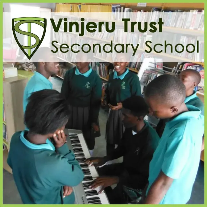 Students in teal uniforms gathered around a keyboard in a library, one student playing while others watch and sing