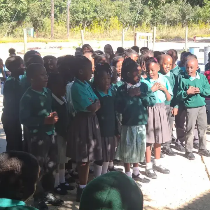 Group of primary school children in green uniforms standing outdoors, some with hands on chest