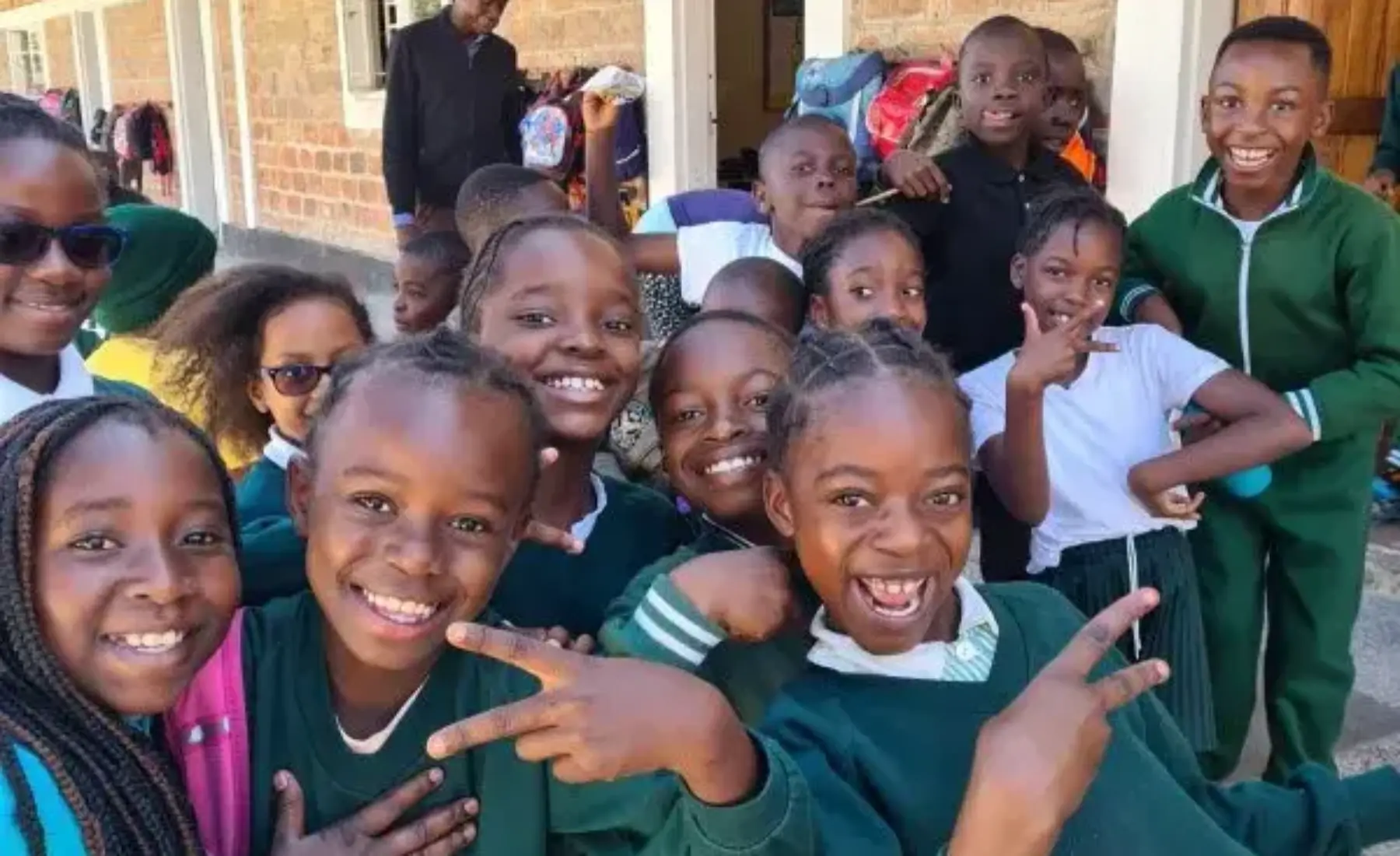 Group of smiling schoolchildren in green uniforms posing outside a brick school building